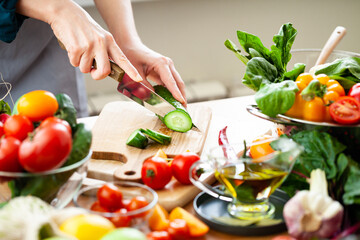 Beautiful young woman slicing green cucumber, preparing delicious fresh vitamin salad. Concept of clean eating, healthy food, low calories meal, dieting, self caring lifestyle. Close up