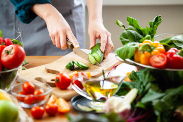 Beautiful young woman slicing green cucumber, preparing delicious fresh vitamin salad. Concept of...