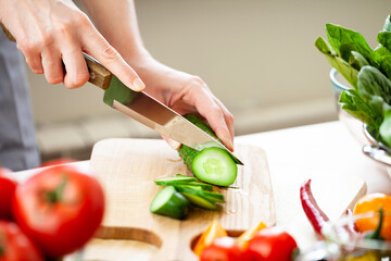 Beautiful young woman slicing green cucumber, preparing delicious fresh vitamin salad. Concept of clean eating, healthy food, low calories meal, dieting, self caring lifestyle. Close up