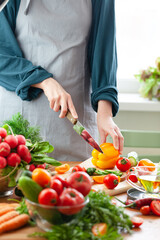 Beautiful young woman slicing yellow pepper, preparing delicious fresh vitamin salad. Concept of clean eating, healthy food, low calories meal, dieting, self caring lifestyle. Close up
