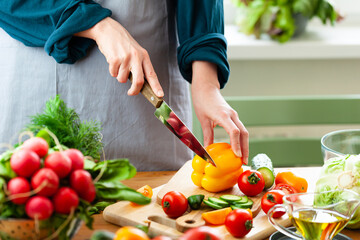 Beautiful young woman slicing yellow pepper, preparing delicious fresh vitamin salad. Concept of clean eating, healthy food, low calories meal, dieting, self caring lifestyle. Close up