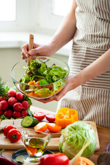Fototapeta na wymiar Beautiful young woman preparing delicious fresh vitamin salad. Concept of clean eating, healthy food, low calories meal, dieting, self caring lifestyle. Colorful vegetables, glass bowl. Close up