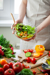Beautiful young woman preparing delicious fresh vitamin salad. Concept of clean eating, healthy food, low calories meal, dieting, self caring lifestyle. Colorful vegetables, glass bowl. Close up