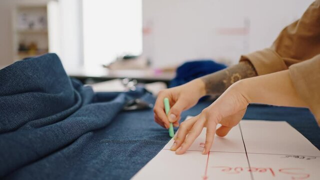 Garment industry. Female tailor outlining cloth pattern on blue fabric at workshop, tracking shot, slow motion