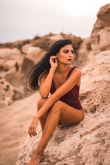 A young brunette Caucasian woman in a maroon swimsuit, sitting on the beach of Cabo de Gata, Nijar. Andalucia, Spain