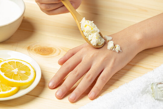 Young woman applying natural lemon scrub on hands against wooden table