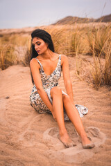 Caucasian brunette stroking her hair in a white floral dress, sitting on the sand on the beach of Cabo de Gata, Nijar. Andalucia, Spain