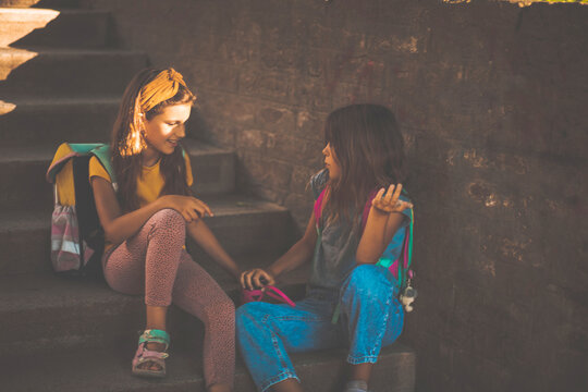 Two little school girls sitting on stairs and talking.