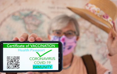 Coronavirus. Blurred senior traveler woman holding straw hat shows health passport on mobile phone, certificate of vaccination of Covid-19