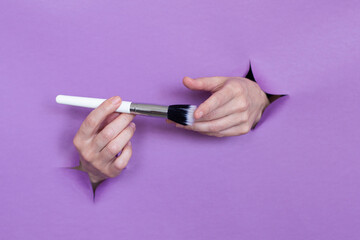 professional makeup brushes in your hands, on a purple background, holes in the background. Space for text