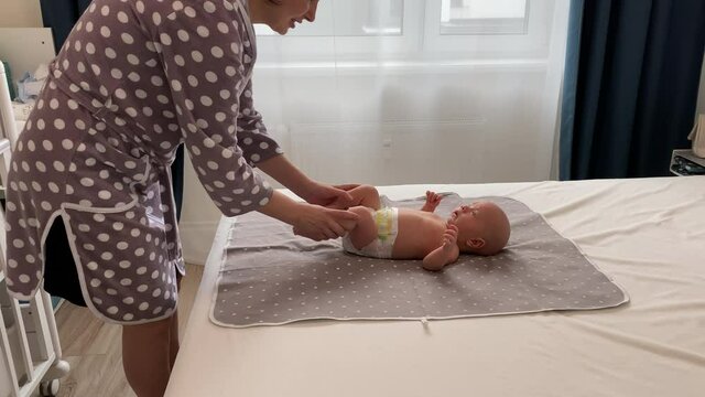 Mother with baby boy doing exercise simple exercises to make baby bones and muscles stronger, newborn infant lying on bed against the window. High quality 4k footage