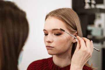 makeup artist applies eyebrow shadow on a beautiful young woman blonde model, face make up concept