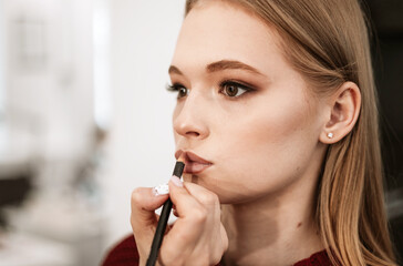 makeup artist paints lips with lipstick with a brush on a beautiful young woman blonde model, face make up concept