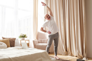 Fototapeta na wymiar Senior bald man in yoga side stretch asana doing exercies alone at home.