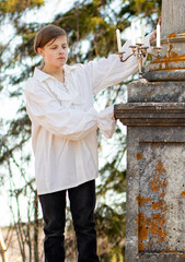 A young man in a white Victorian shirt against the background of a marble column in a candlestick