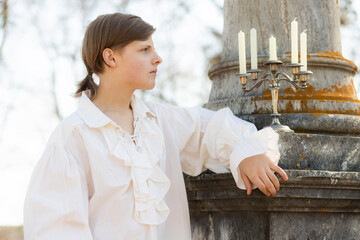 A young man in a white Victorian shirt against the background of a marble column in a candlestick