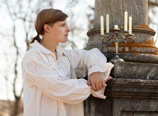 A young man in a white Victorian shirt seated at a marble monument