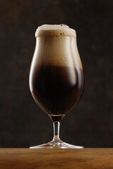 Glass of Dark Beer With Overflowing Foam Head on Dark Gray Background. 