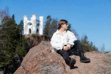Boy sitting on a granite rock against the background of a blue sky and a white castle