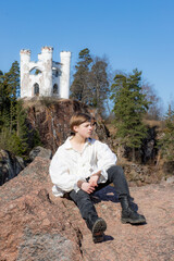 Boy sitting on a granite rock against the background of a blue sky and a white castle