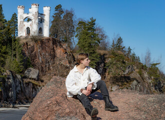 Boy sitting on a granite rock against the background of a blue sky and a white castle