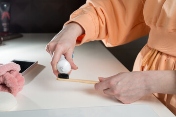 Closeup female hand is holding ecological bamboo brush with whitening toothpaste. woman is preparing going to clean teeth. Tool for oral care. Personal hygiene product concept