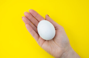 White egg in woman hand on the yellow background. Copy space. Minimalism, original and creative...