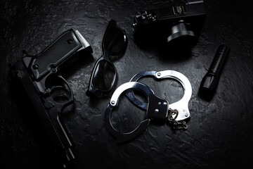 Black gun, flashlight, glasses, camera and Police metal real handcuffs lie on the black background....