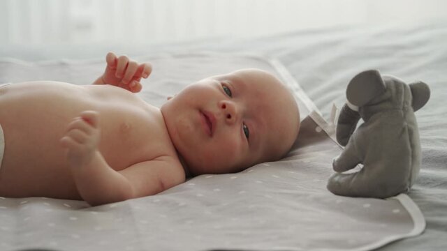 Mother with baby boy doing exercise simple exercises to make baby bones and muscles stronger, newborn infant lying on bed against the window. High quality 4k footage