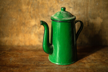 A green enameled metal teapot on a wooden table.