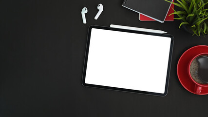 Modern dark workspace with digital tablet, stylus pen, earphone and coffee cup on black leather.