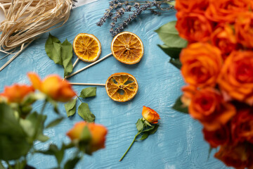 Fototapeta na wymiar A flower made from dried orange slices with orange rose blossoms with lavender on blue wooden background