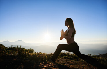 Side view of slim woman in black sportswear doing yoga on fresh air. Concept of yoga time on nature with beauty landscape.