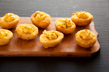Homemade Deep-fried Deviled Eggs with Paprika on a Rustic Wooden Board, side view.