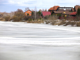 country pond, covered with a crust of spring ice with cozy houses in the distance