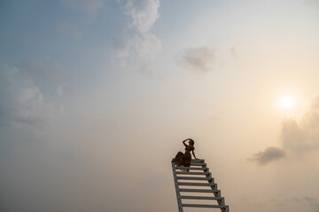 Woman in brown dress sitting on the staircase, sunset moment. © marchsirawit