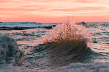 winter landscape from the sea shore, blurred wave slags against frozen ice cubes, blurred sunset color background