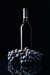 Bottle of red wine and a bunch of grapes on a black reflective background.