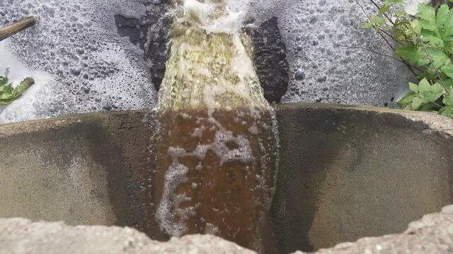 Brown swamp water full of organic substances flows down the pipe and forms a plentiful foam, biofouling