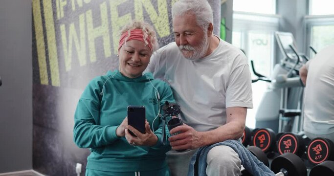 Elderly couple at the gym use a smartphone to read the news and surf the social networks