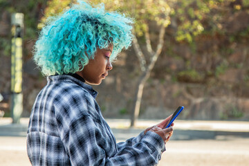 young afro american girl with blue hair looking at mobile phone