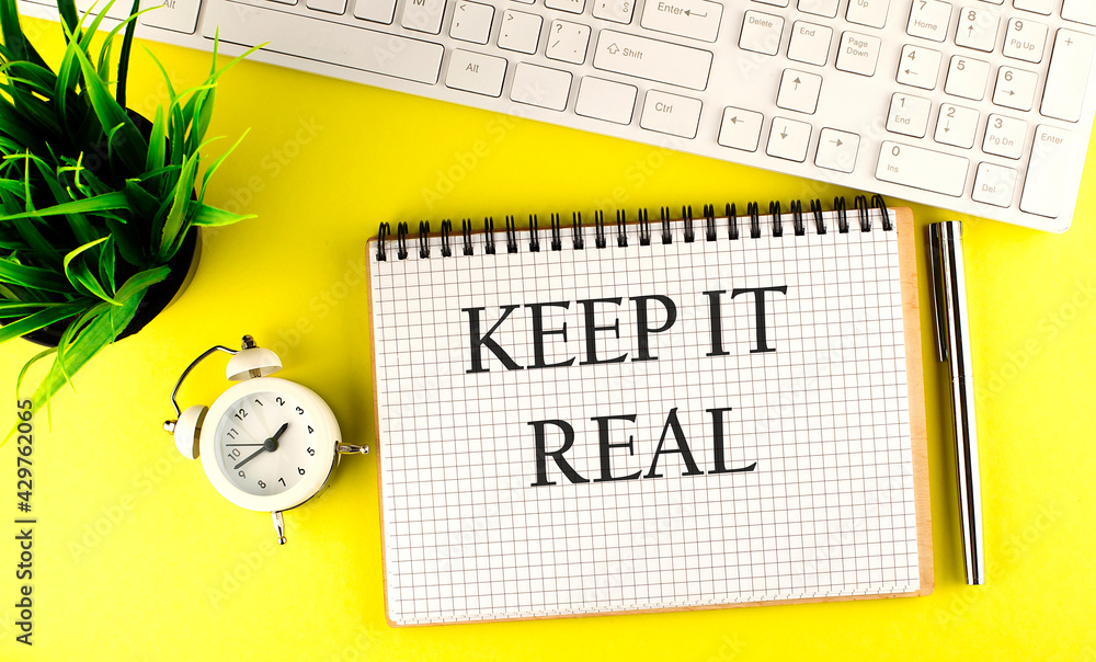 Poster keep it real text on notebook with keyboard , pen and alarm clock on the yellow background