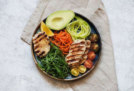 Salad with grilled chicken breast, arugula, avocado, carrots and zucchini, balanced clean eating, top view. Healthy lunch bowl.
