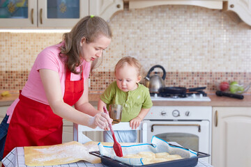 A young woman teaches a child to cook pastries. Greases the pies in the baking tray with a cooking brush.