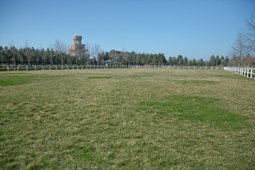 A white fence with green gardens . Horse racecourse field . Large farmland and ranch protection background . Green pastures of horse farms. Country summer landscape. White fence is a long way.