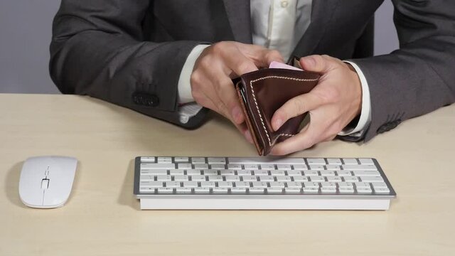 Man in official costume counts money in brown leather wallet and puts it in inner pocket of his suit, businessman, cash, sitting in office, white computer keyboard and mouse. Close up, 4K Ultra HD.