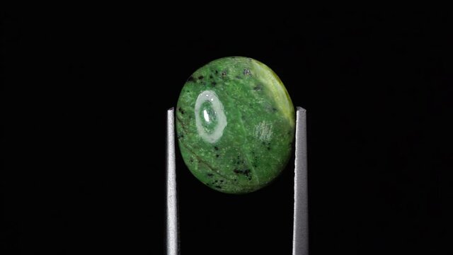 natural green opal gemstone in the tweezer on the background