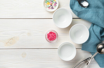 Empty white bowls, an ice cream spoon and confectionery sweets on a white wooden background.