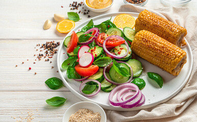 Fresh vegetable salad and roasted corn on a light background with spices, basil and lemon.