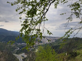 Discovering the mountains around Genoa. Panoramic view to the city. Grey sky in the background. First green leaves in spring.